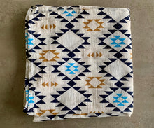 Load image into Gallery viewer, Organic Cotton Muslin Swaddle cloth with geometric Aztec print design in blue/black/gold. Cloth is folded on marble table.
