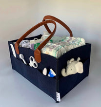 Load image into Gallery viewer, navy blue nappy caddy organiser with brown pu leather handles. shown filled with baby changing essentials such as nappies, wipes, outfits, muslins, toy, teething gel, comb etc
