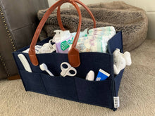 Load image into Gallery viewer, navy blue nappy caddy with brown leather handles filled with baby changing essentials. shown on neutral carpet.
