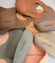 Load image into Gallery viewer, Silicone Bib BPA Free in light peach/butternut squash colour and 4 buttons with large crumb catcher scoop. Displayed with other colours for comparison.
