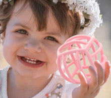 Load image into Gallery viewer, Toddler girl holding pink blush silicone teething ball and smiling.
